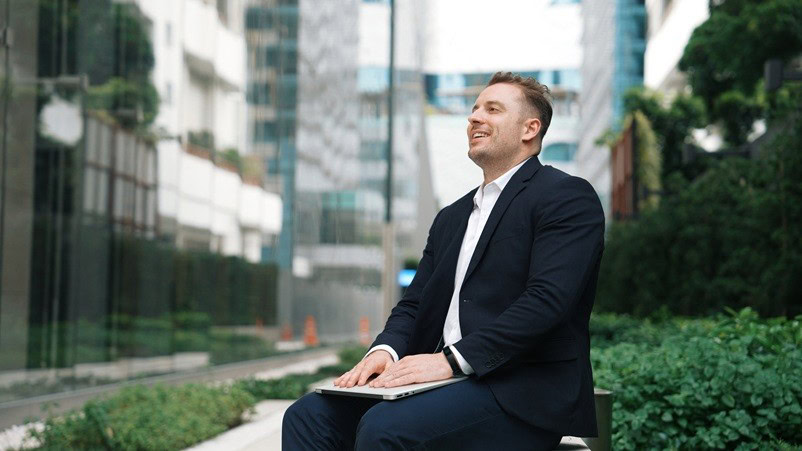lawyer sitting outside in a business courtyard with a closed laptop, smiling
