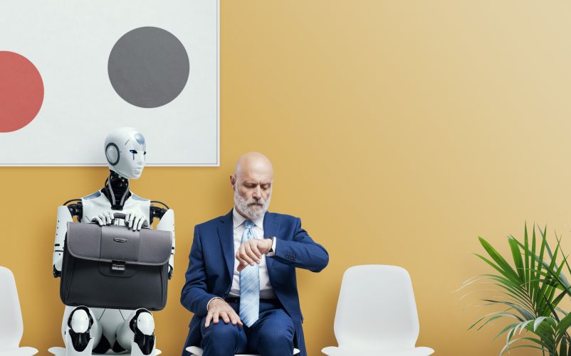 professional man sitting in a waiting room next to a human-like robot