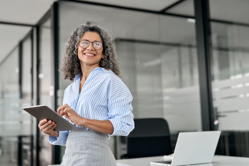 mature professional woman with curly hair and glasses in a modern office setting