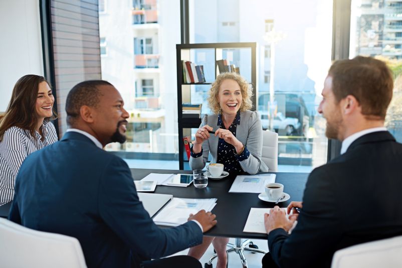 a group of diverse professionals laughing and talking around a conference table